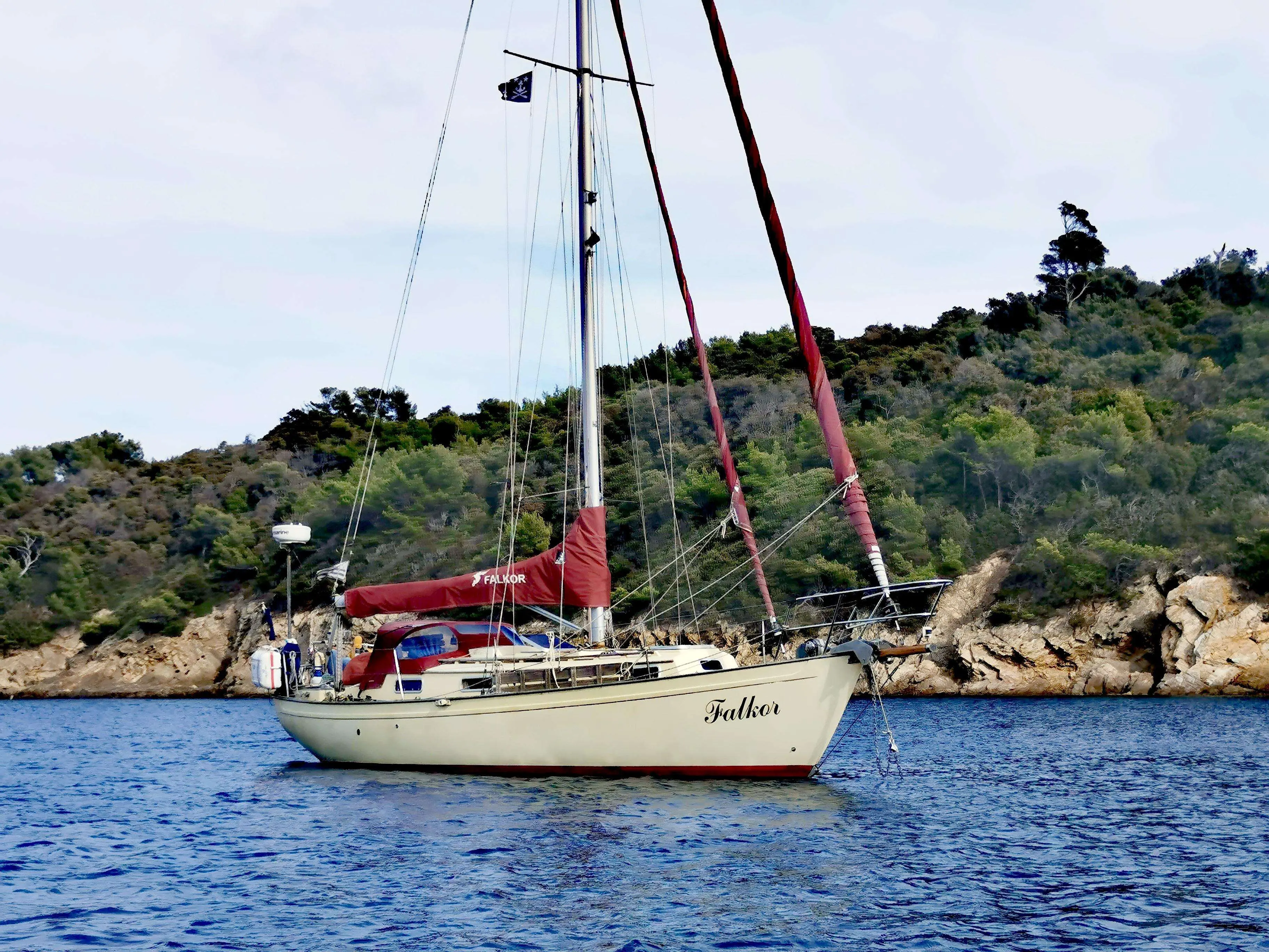 Victoria Yachts Victoria 34 — Voilier vu de profil sur l’eau, voiles ferlées, devant une côte boisée.