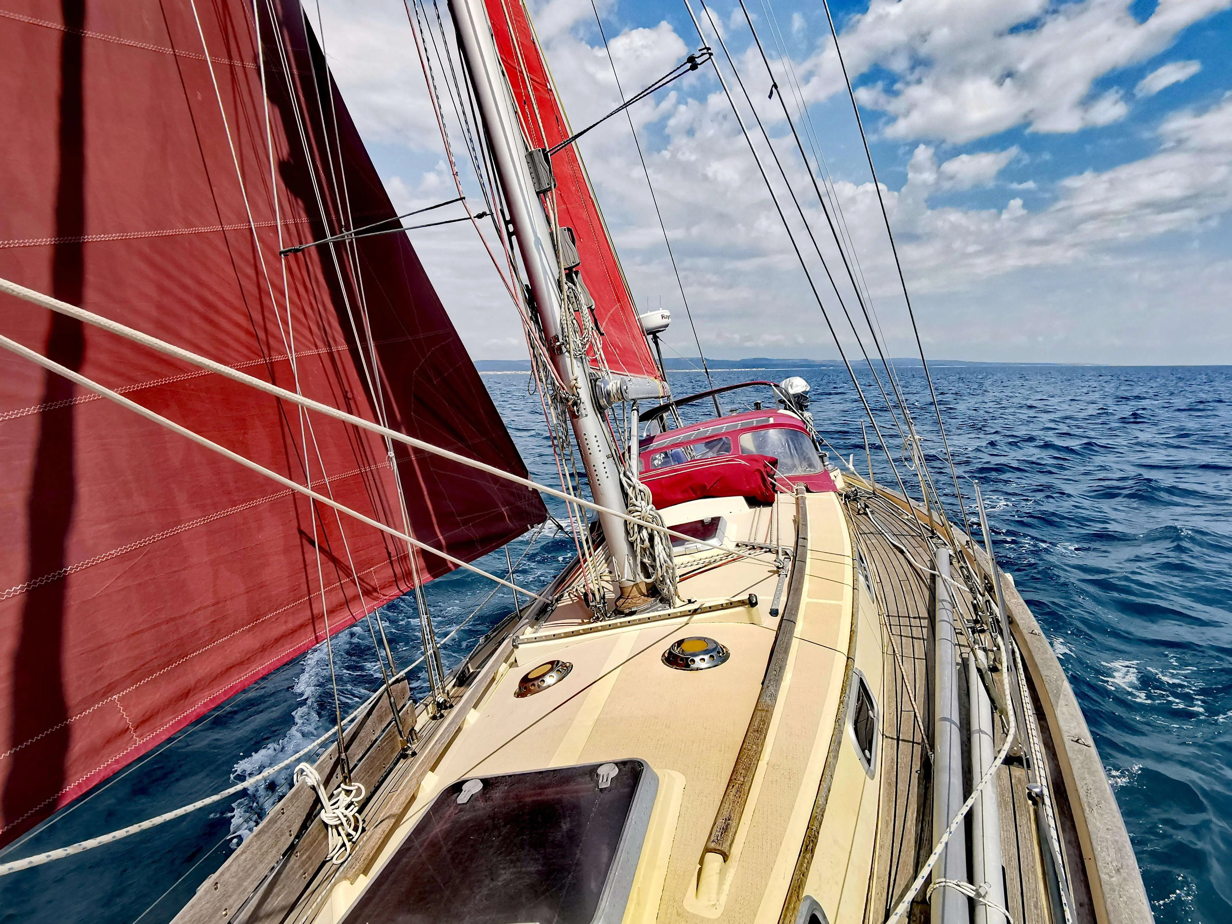 Victoria Yachts Victoria 34 — Voilier en navigation, vu depuis le pont avec ses voiles rouges déployées.