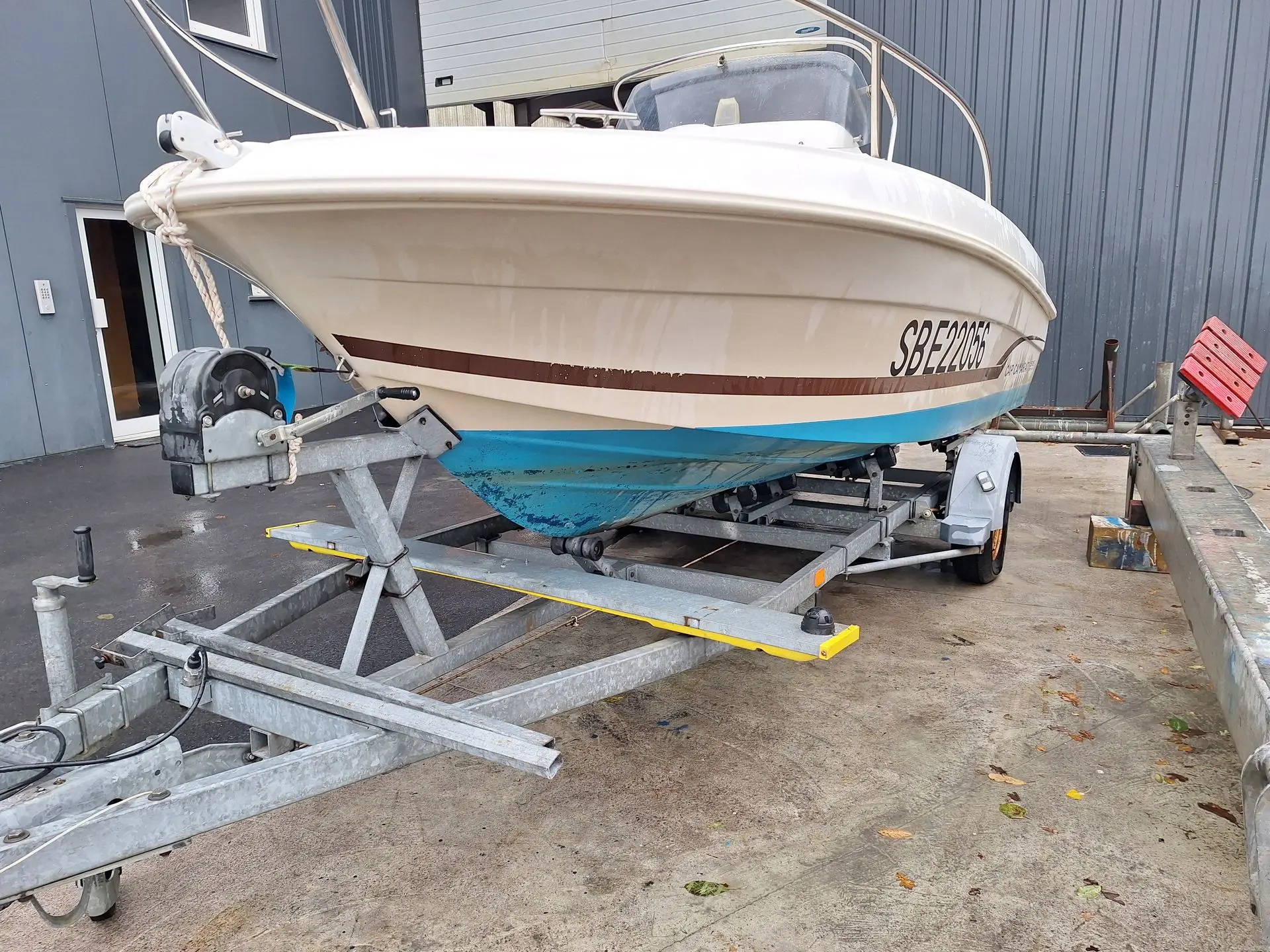 Jeanneau Cap Camarat 505 — Bateau à moteur blanc et bleu posé sur une remorque devant un bâtiment.