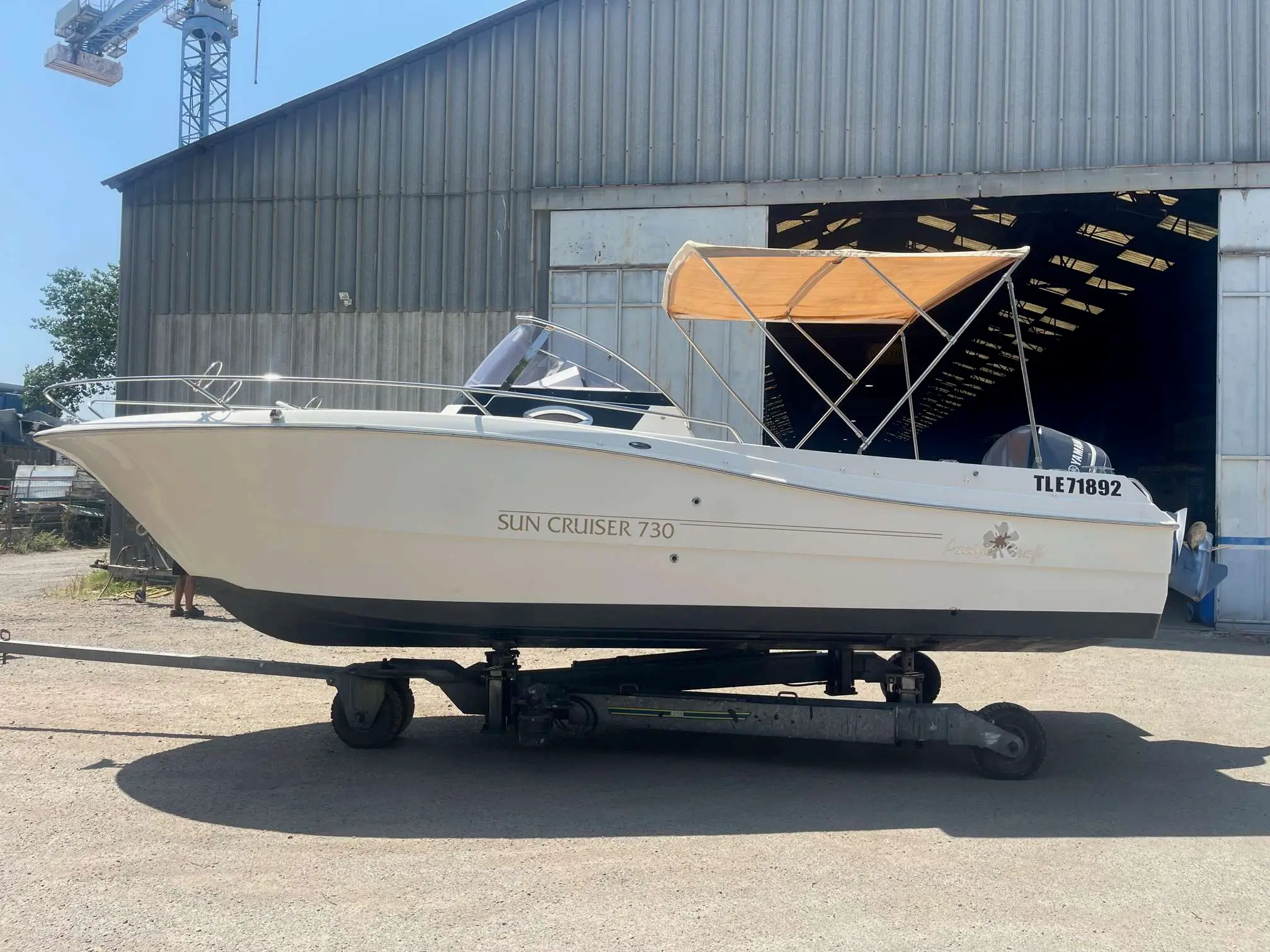 Pacific Craft 730 SC — Bateau à moteur blanc photographié de profil sur sa remorque devant un hangar.