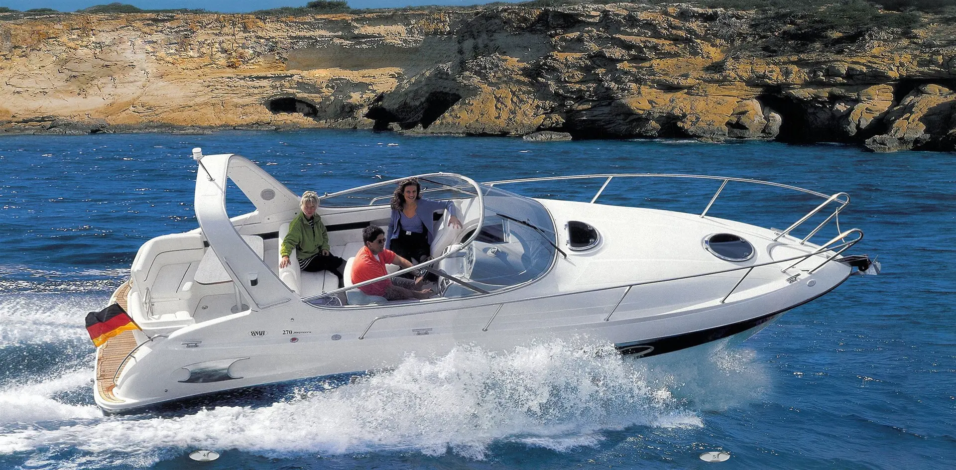 Bavaria 270 — Bateau à moteur blanc naviguant devant une côte rocheuse, avec trois personnes à bord.
