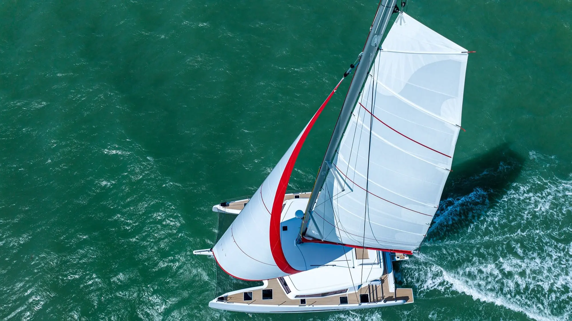 Neel Trimarans Neel 52 — Vue aérienne d’un trimaran à voile naviguant sur une mer turquoise.