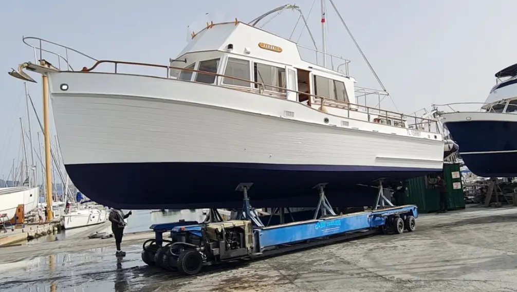 Grand Banks 42 Motoryacht — Bateau à moteur blanc et bleu présenté sur une remorque dans un chantier naval.