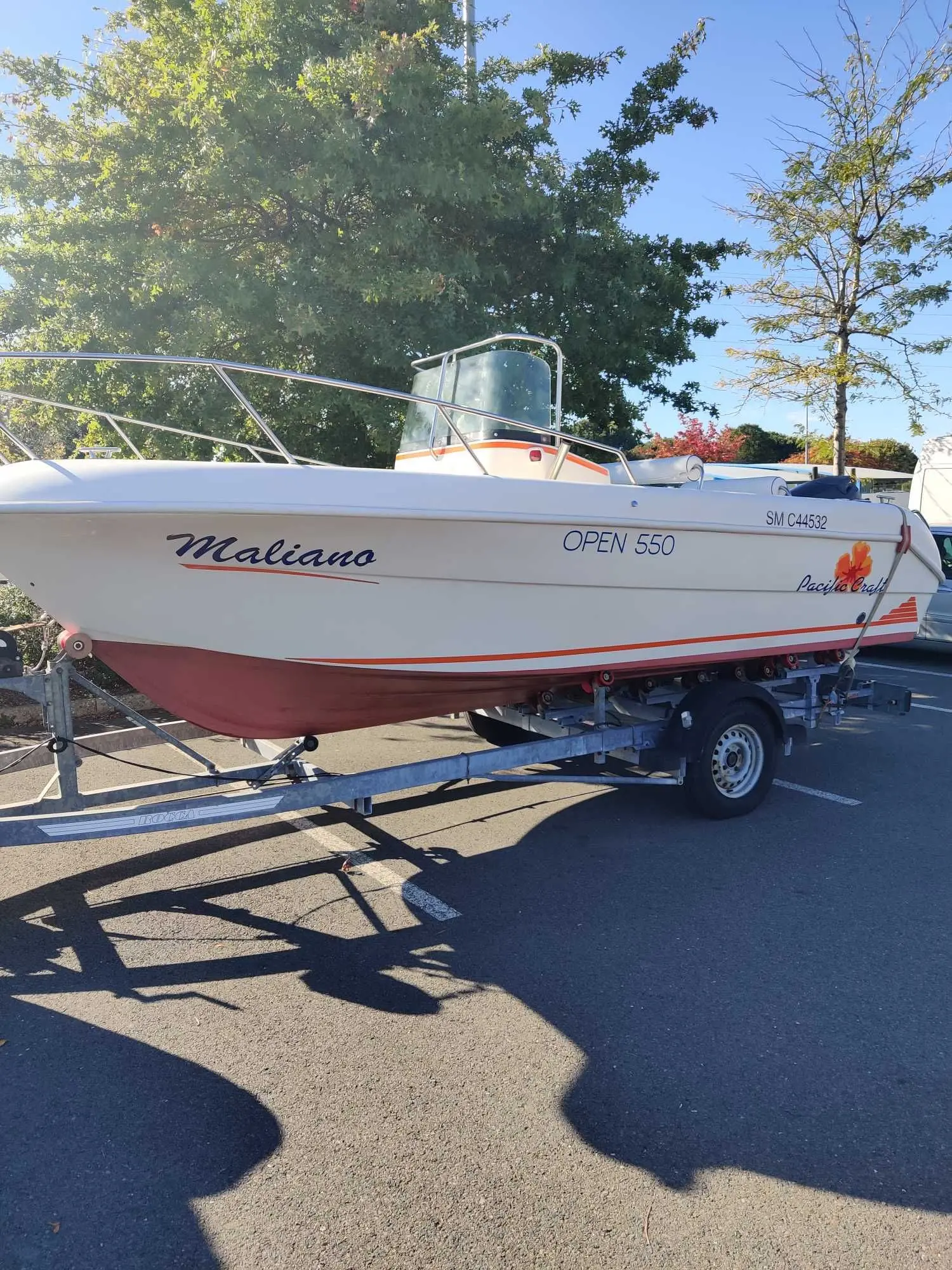 Pacific Craft 550 Open — Bateau à moteur blanc sur remorque, photographié de profil sur un parking.