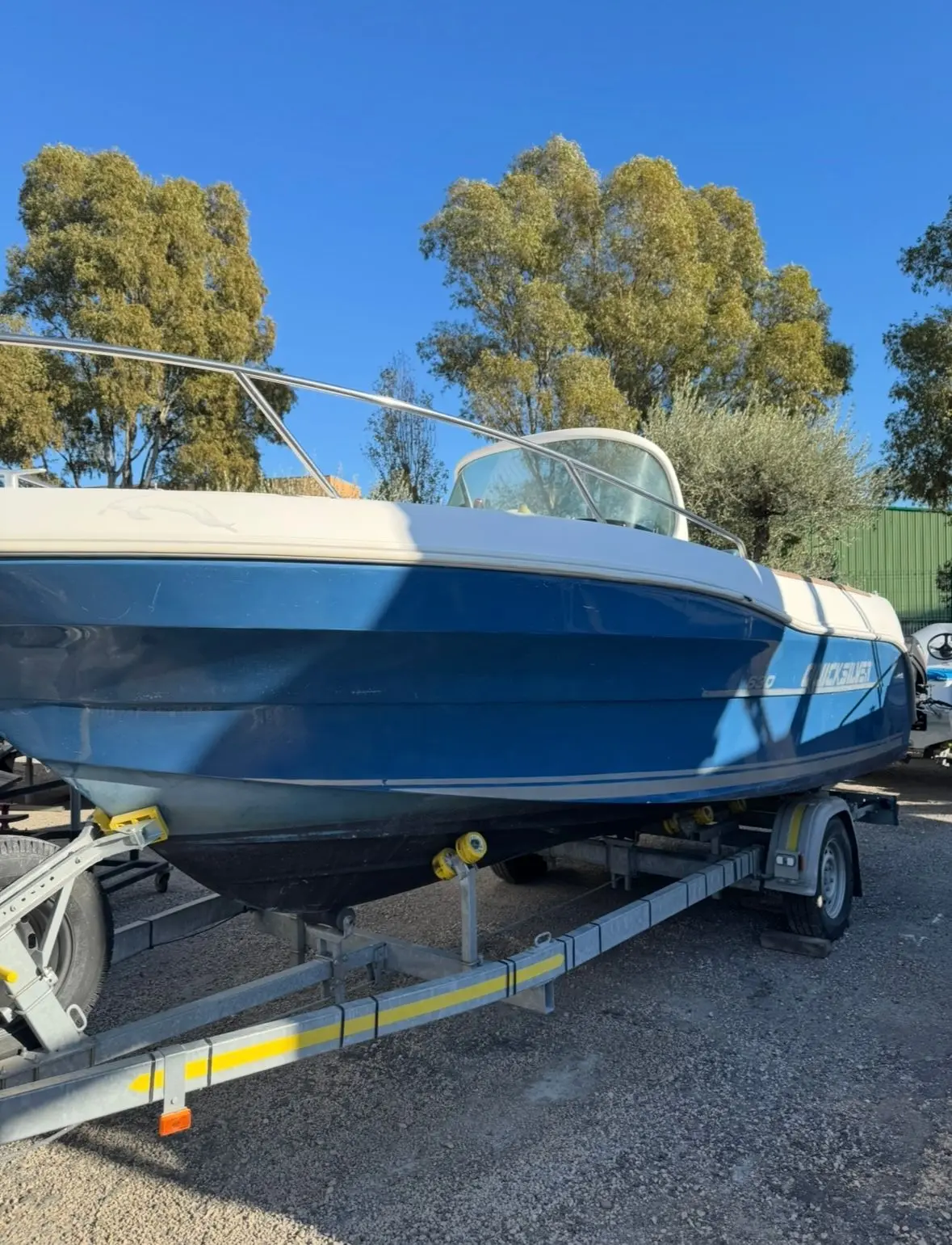 Quicksilver 630 Open Commander — Bateau à moteur bleu et blanc présenté sur sa remorque, à terre.