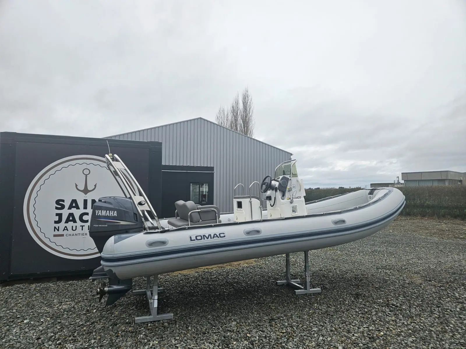 Lomac 580 OK — Bateau pneumatique blanc exposé sur bers devant un bâtiment, par temps couvert.