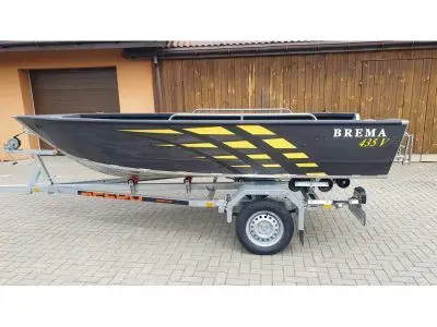 Brema 435V Fishing — Bateau à moteur gris et jaune présenté sur une remorque devant un bâtiment.