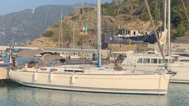 Dufour 455 — Voilier blanc amarré dans un port, vu de profil, avec des montagnes en arrière-plan.