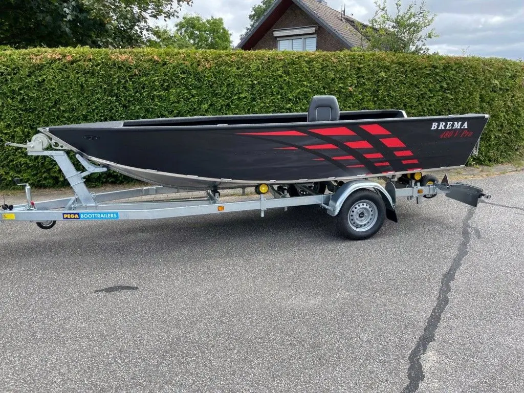 Brema 480V Fishing Pro — Bateau noir et rouge présenté sur sa remorque, vu de profil devant une haie.
