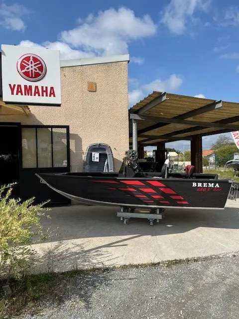 Brema 480V Pro Bass — Bateau noir et rouge exposé sur remorque devant un établissement Yamaha.