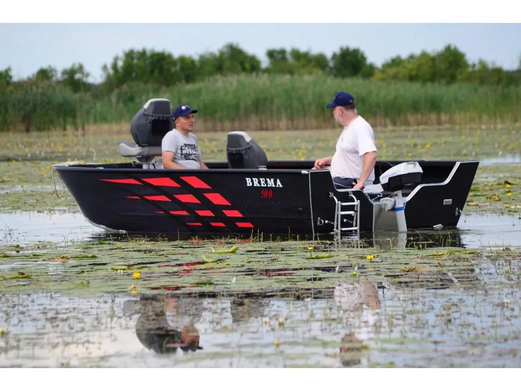 Brema 500 Fishing Pro — Vue latérale d’un bateau noir et rouge naviguant sur un plan d’eau couvert de nénuphars.