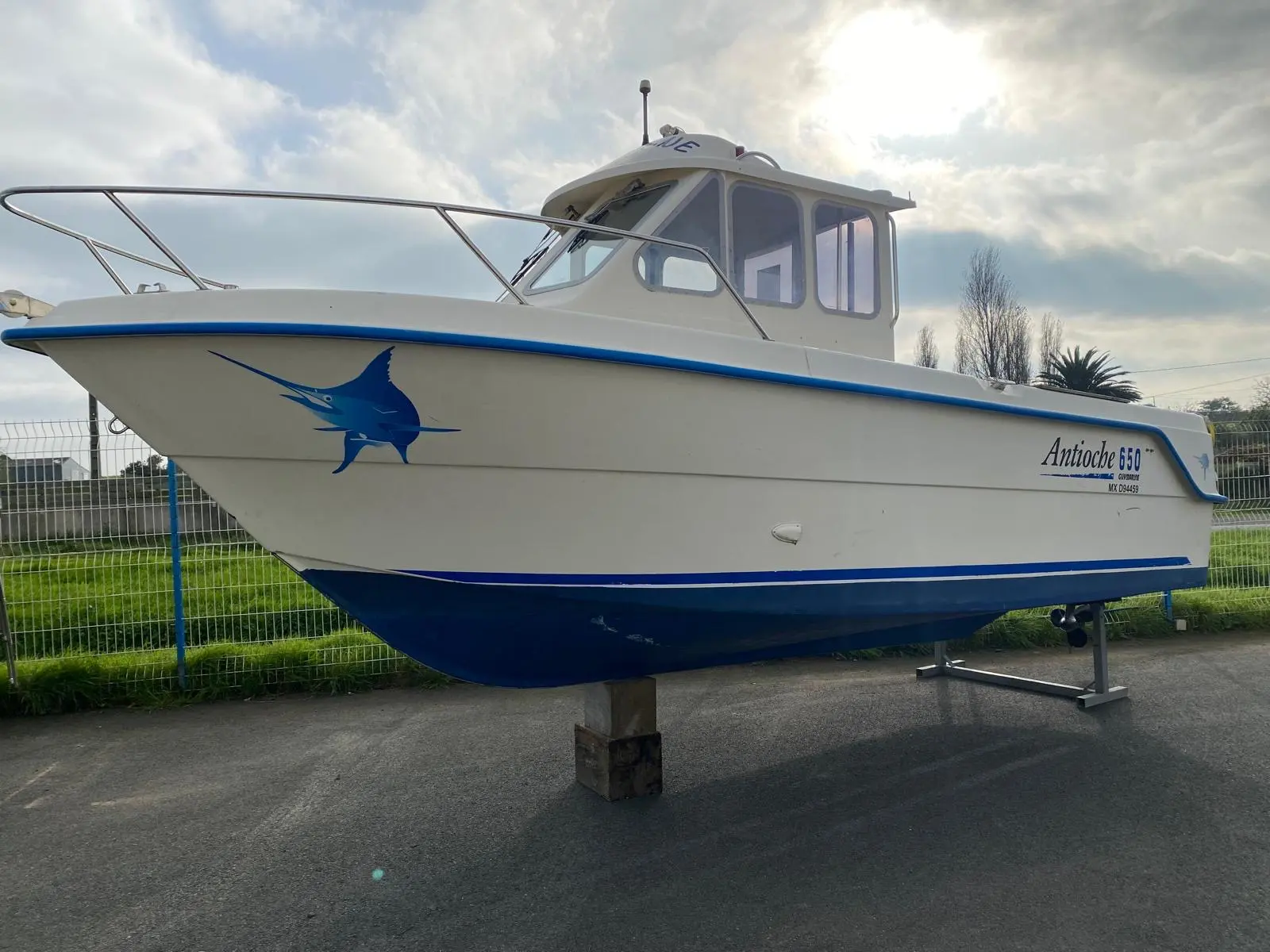 Guymarine Antioche 650 — Bateau à cabine vu de profil sur bers, à terre, devant une clôture.