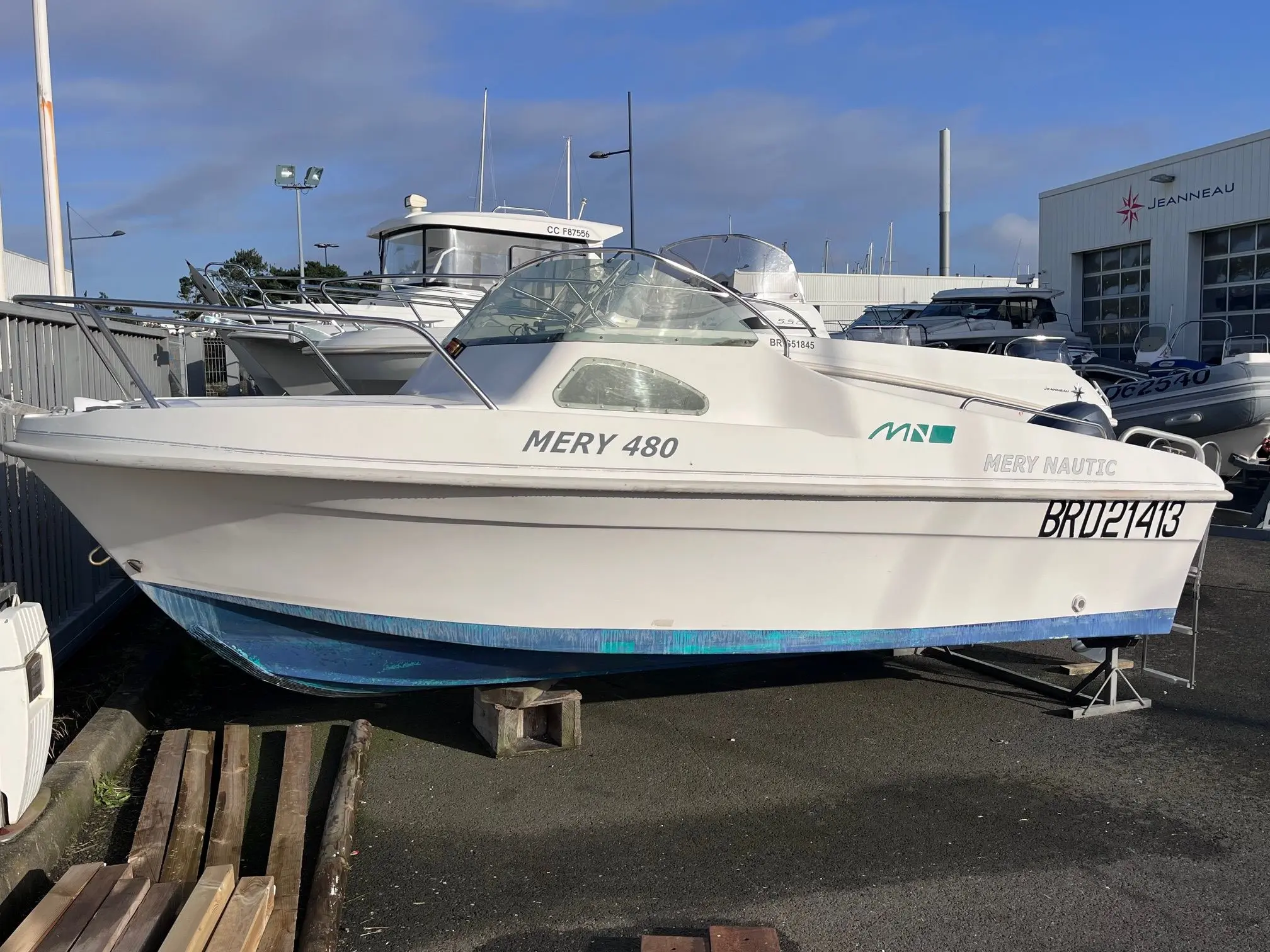 Mery Nautic 480 — Bateau blanc vu de profil sur remorque, stationné devant un concessionnaire nautique.