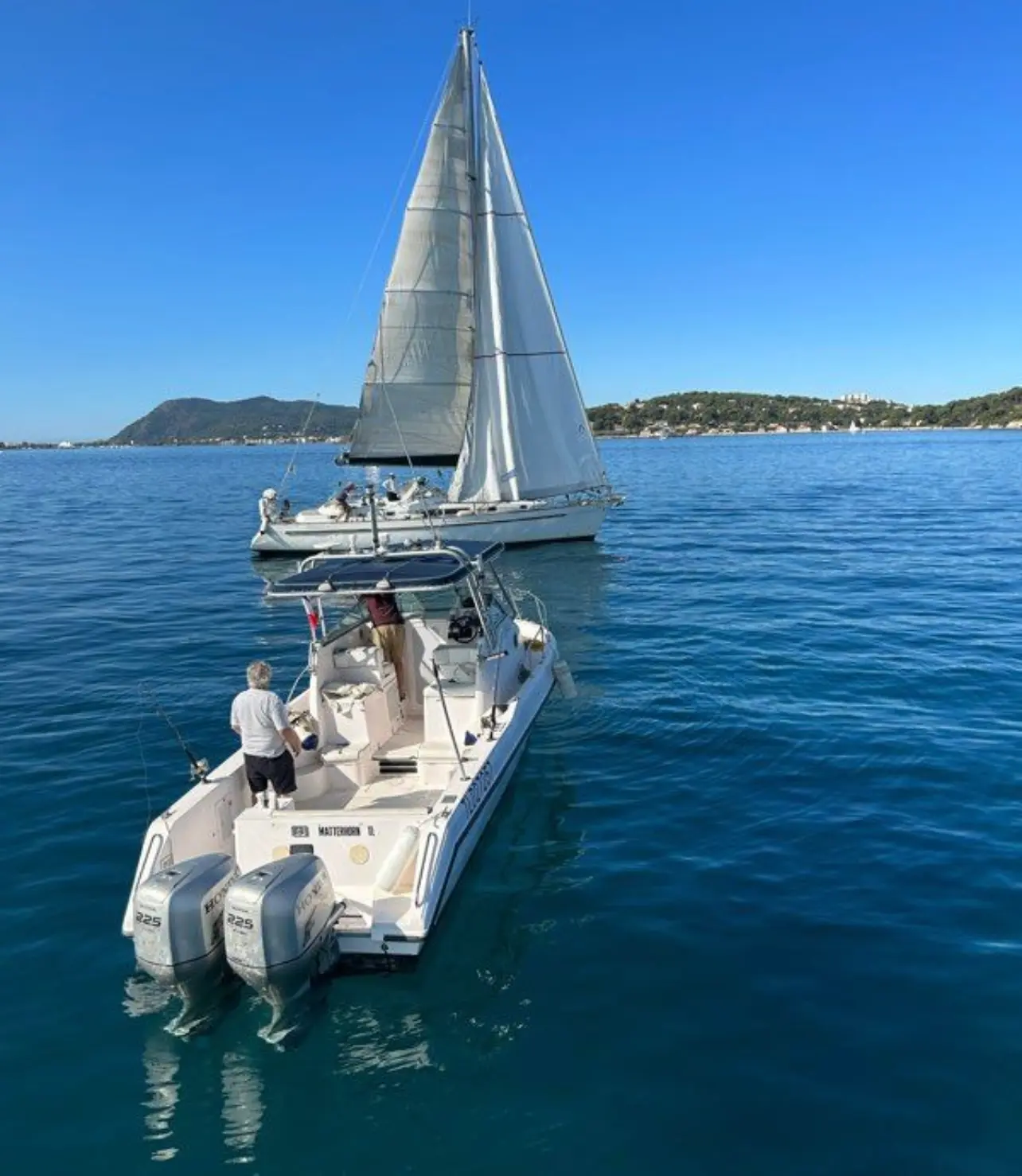 Gulf Craft 31 WA — Bateau à moteur vu de l’arrière, avec deux personnes à bord et un voilier en arrière-plan.