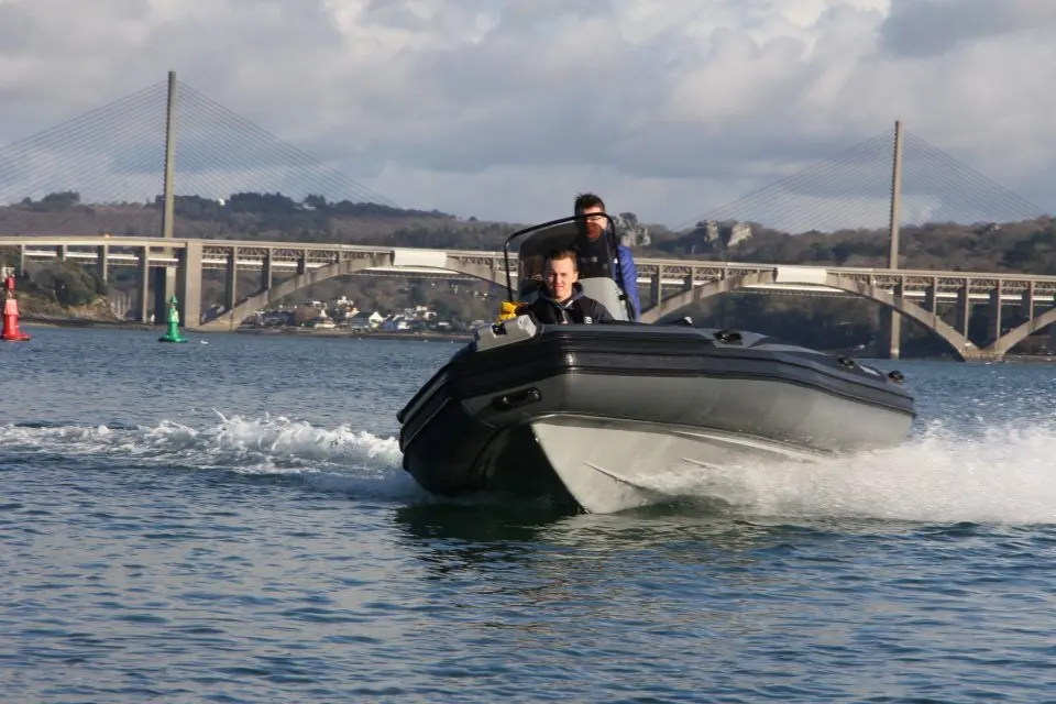 Adventure Vesta 585 Profish — Bateau semi-rigide naviguant devant un pont, avec deux personnes à bord.