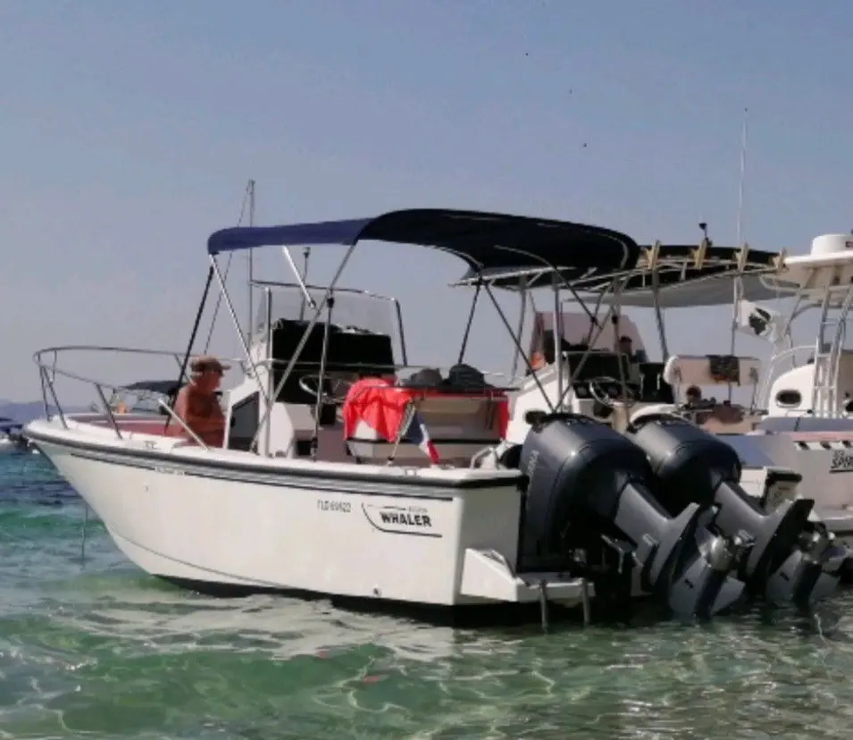 Boston Whaler 24 Outrage — Bateau à moteur blanc à double motorisation, sur l’eau, avec des bateaux voisins.