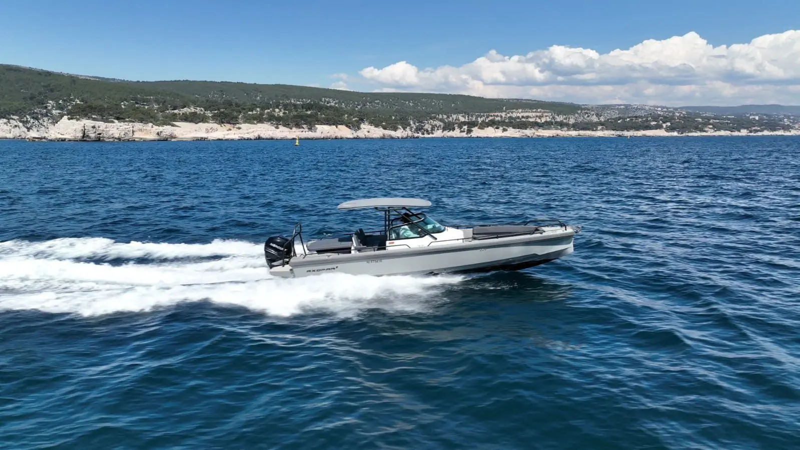 Axopar 28 T Top — Bateau à moteur gris naviguant au large d’une côte rocheuse.