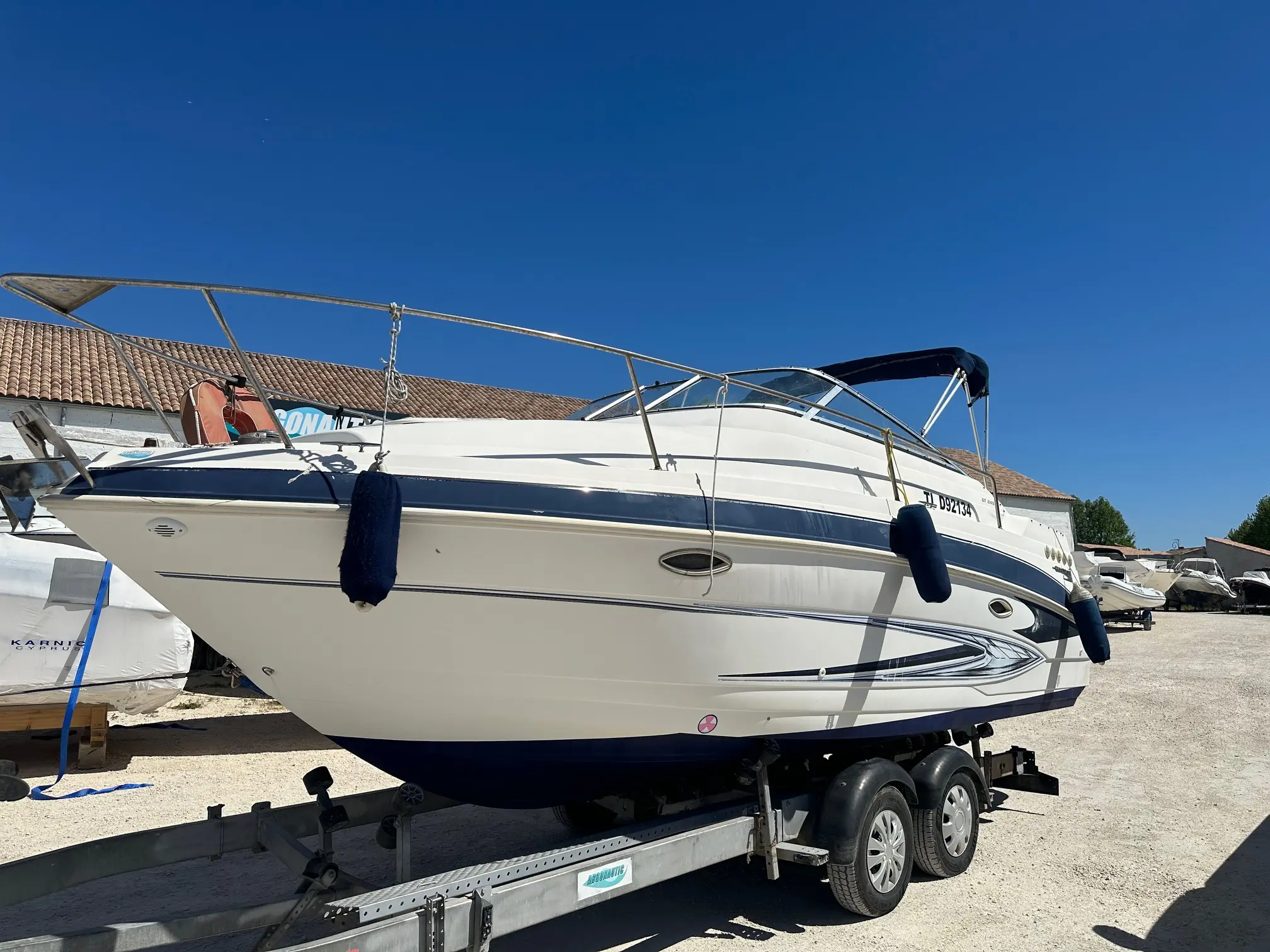 Glastron GT 249 — Bateau à cabine blanc et bleu photographié sur sa remorque dans un chantier nautique.