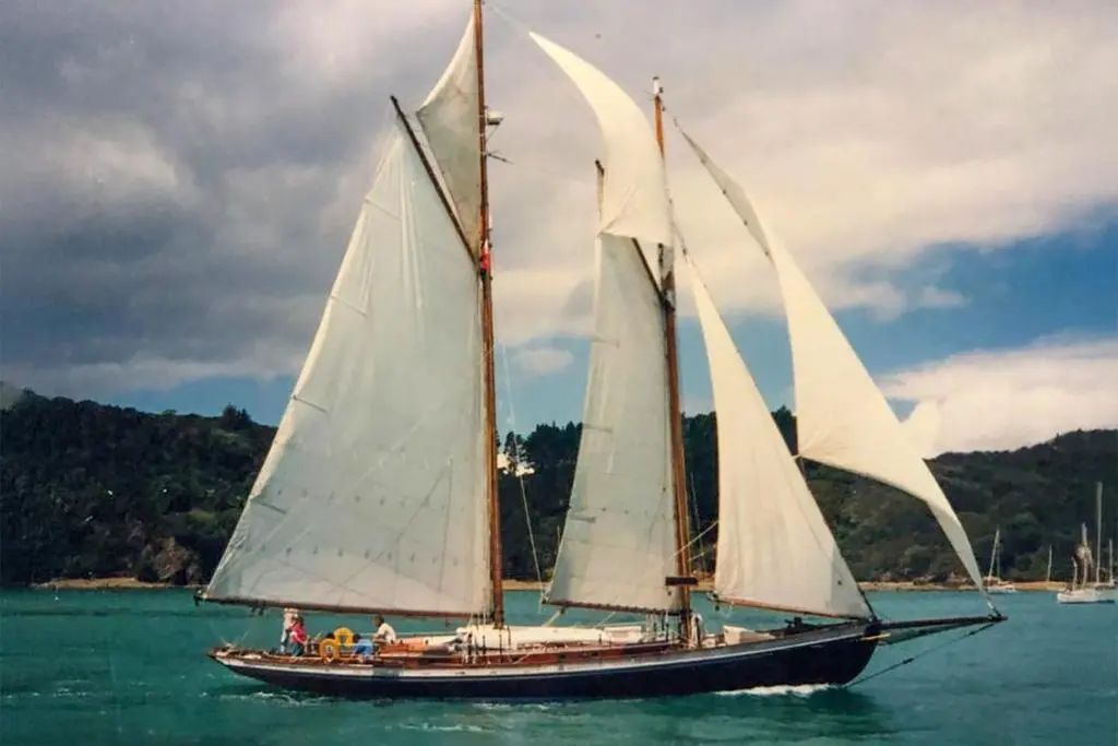 Goelette Aurique — Goélette à trois mâts naviguant près d’une côte boisée.