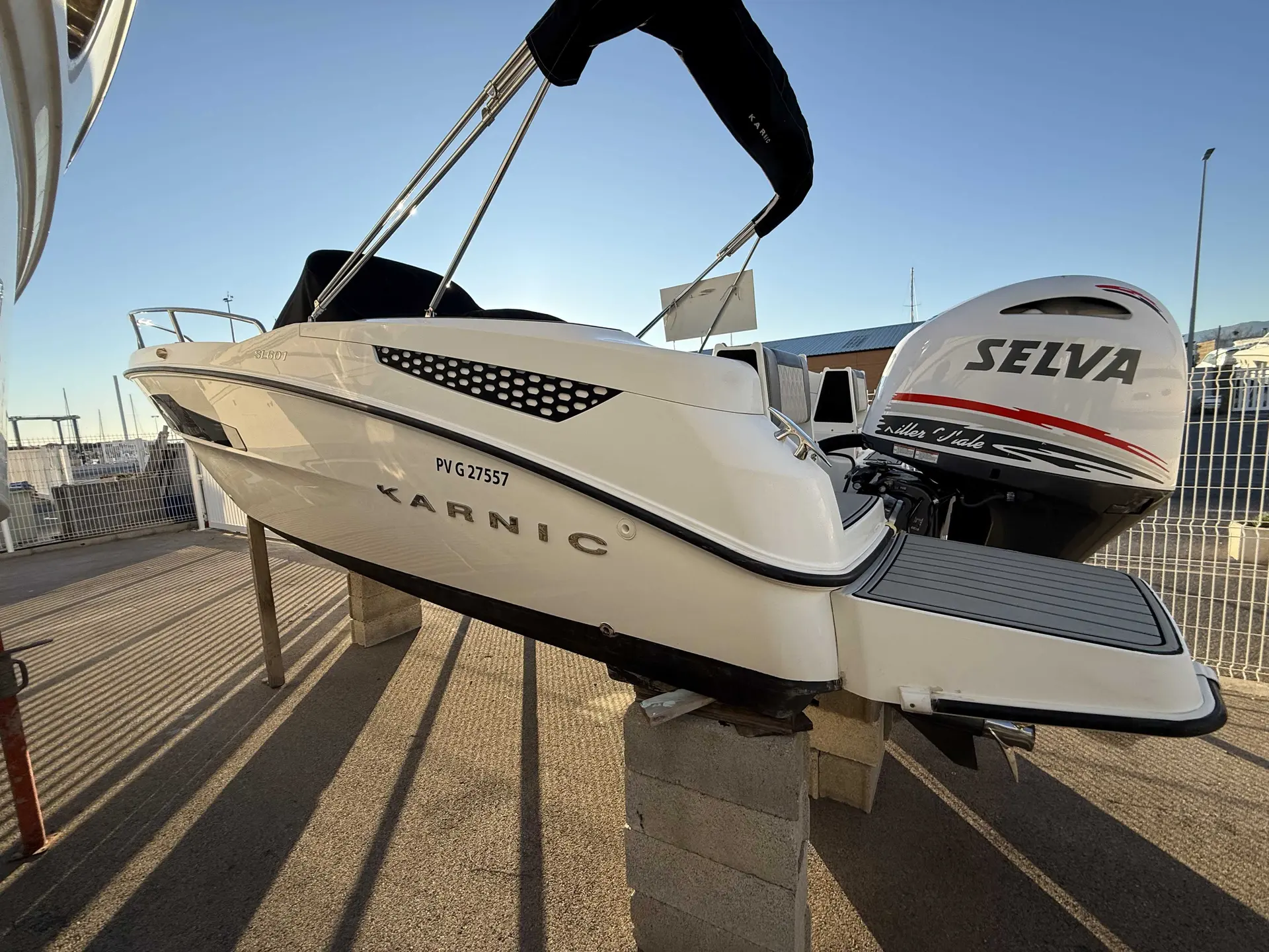 Karnic SL601 — Bateau blanc vu de trois quarts arrière, exposé sur berceau avec moteur hors-bord.