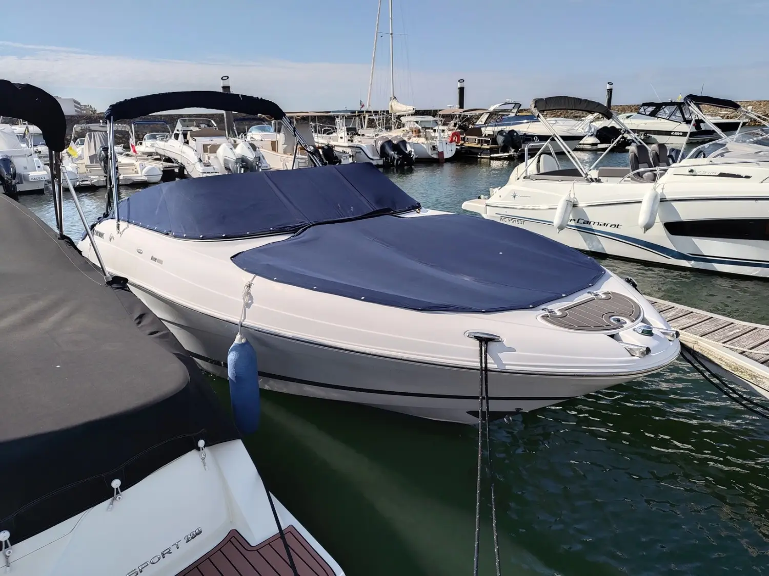 Four Winns Horizon 260 — Bateau de plaisance blanc amarré dans un port, avec tauds bleus et bateaux voisins.