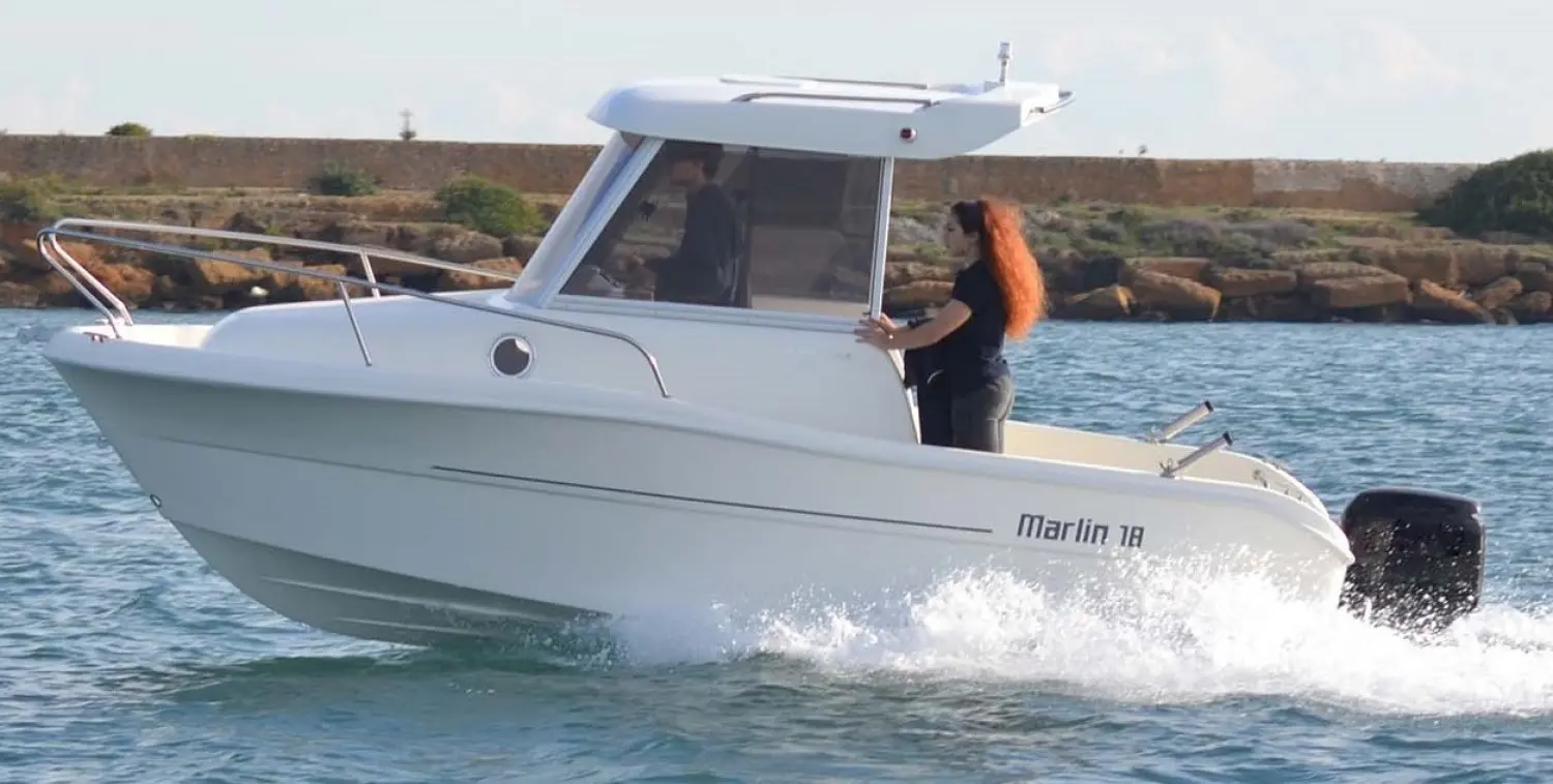 Mingolla Marlin 18 — Bateau à moteur blanc naviguant près d’une côte rocheuse, avec une personne à bord.