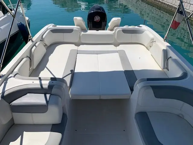 Bayliner E7 — Vue du cockpit arrière avec banquettes en L, bain de soleil et moteur hors-bord.