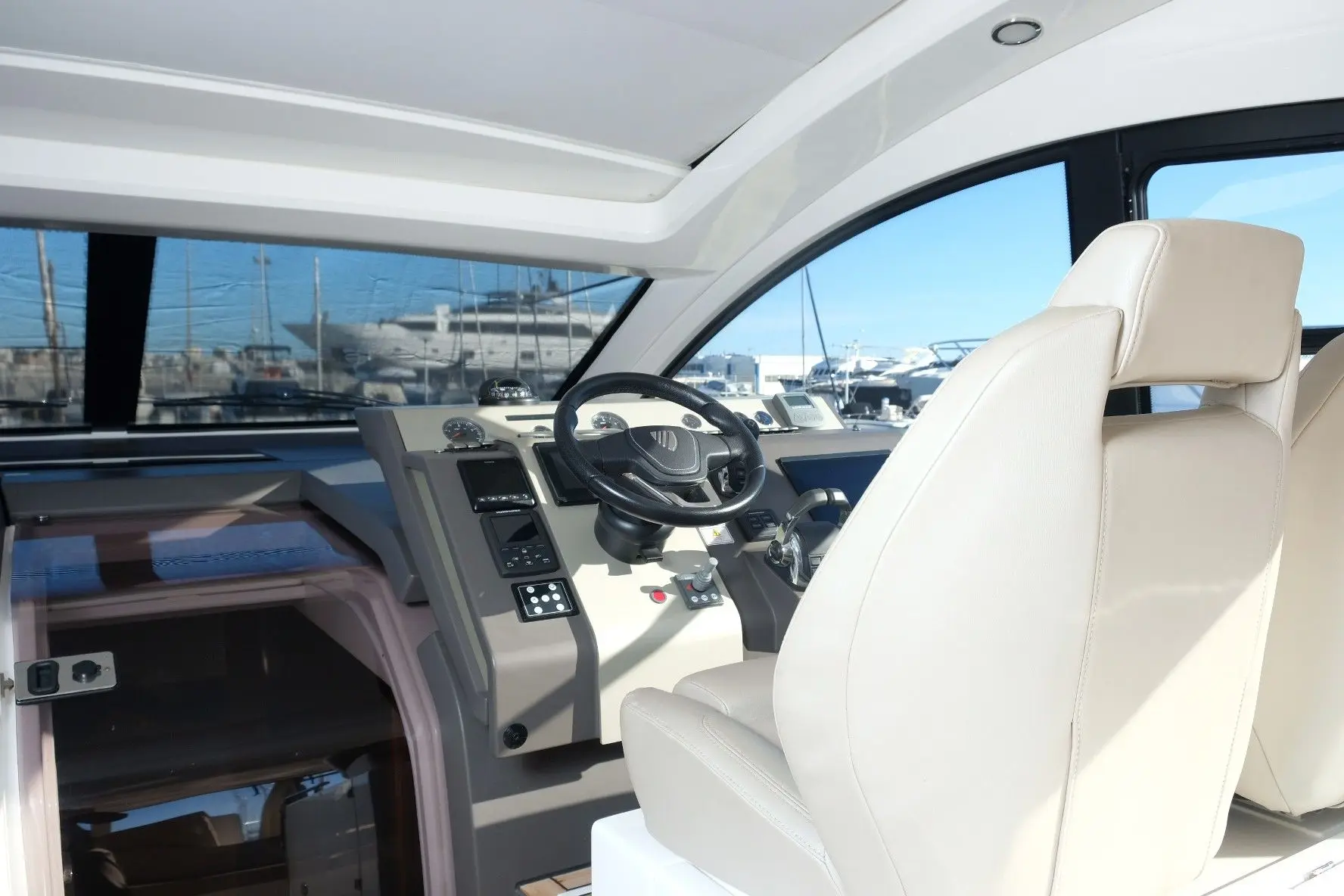 Fairline Targa 50 Open — Poste de pilotage intérieur avec tableau de bord et sièges face à la marina.