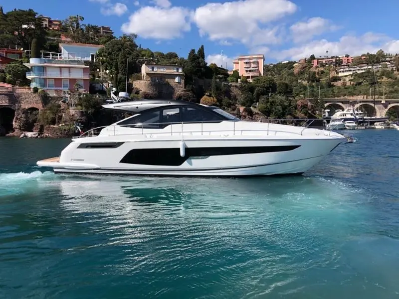 Fairline Targa 50 Open — Vedette à moteur blanche filmée de profil près d’un rivage résidentiel.