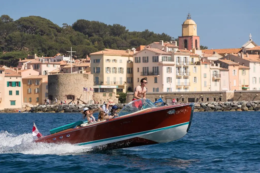Riva Ariston — Bateau à moteur verni naviguant devant un village méditerranéen.