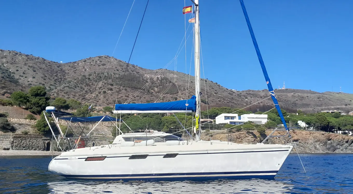 Jeanneau Espace — Voilier blanc vu de profil sur l’eau, au pied d’une côte rocheuse.