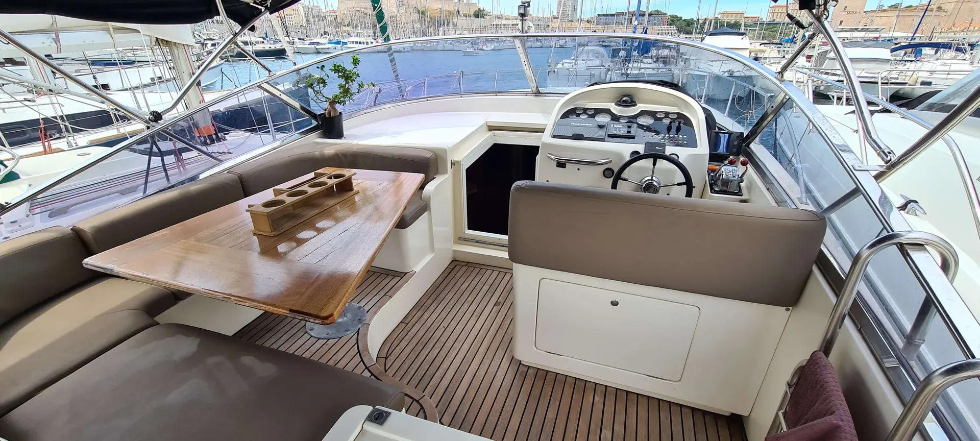 Baia Zero 43 — Vue du cockpit avec salon, table, poste de pilotage et marina en arrière-plan.