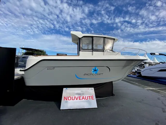 Pacific Craft 650 — Bateau à moteur exposé à terre, photographié de profil avec sa cabine fermée.