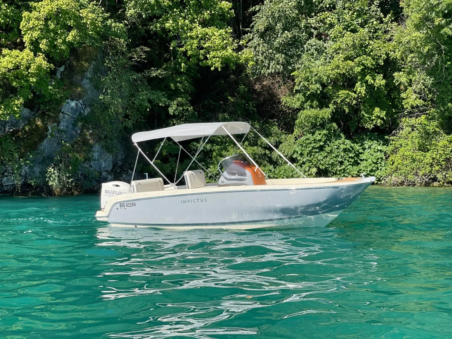 Invictus 200 FX — Bateau à moteur blanc naviguant sur une eau turquoise devant une rive boisée.