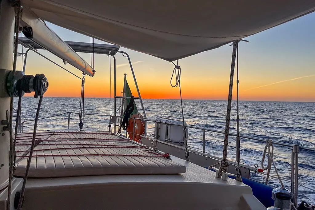 Amel Super Maramu 2000 — Vue du pont arrière d’un voilier au coucher du soleil, en mer.