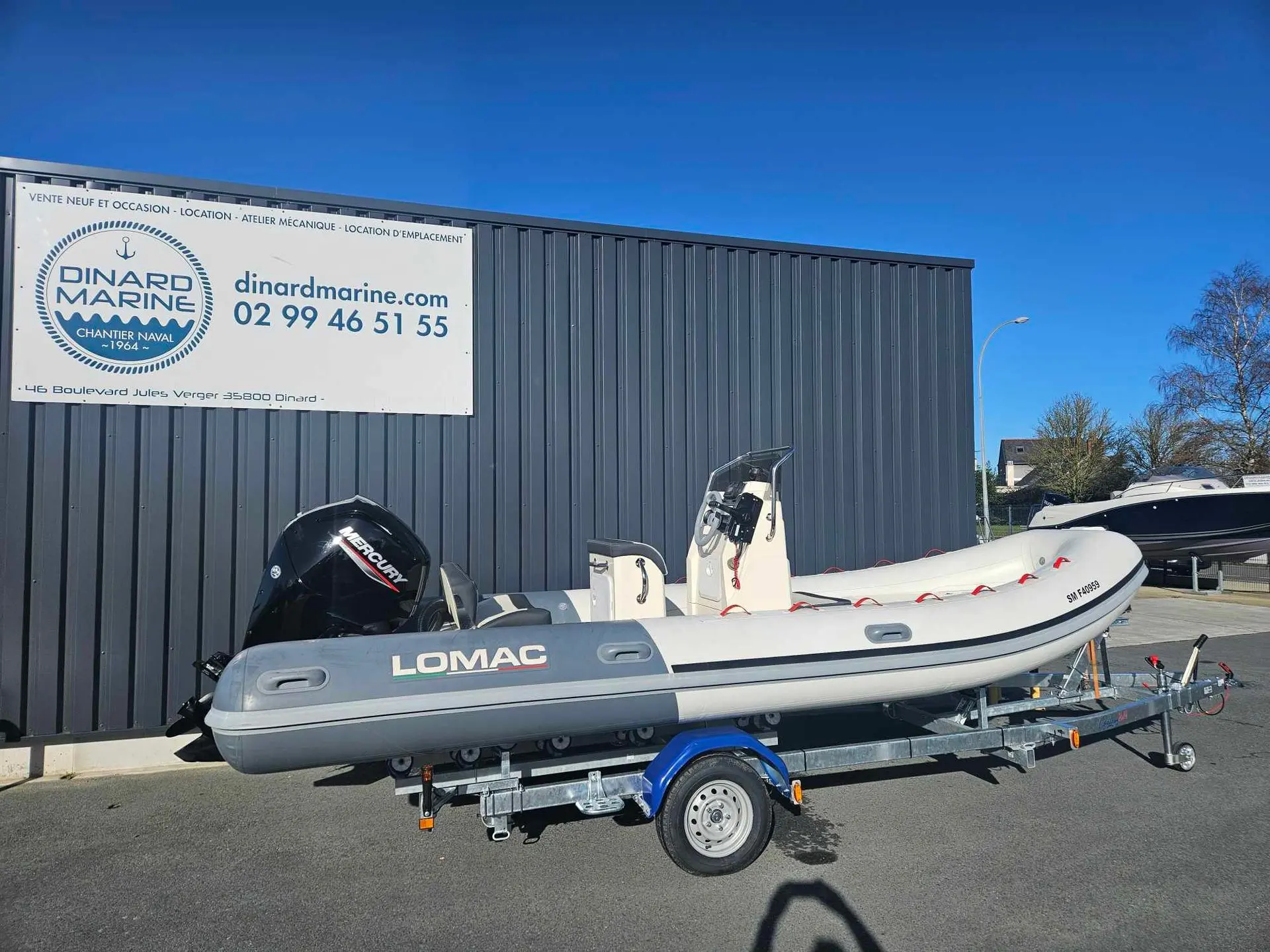 Lomac 580 OK — Semi-rigide blanc sur remorque, photographié devant un bâtiment nautique.