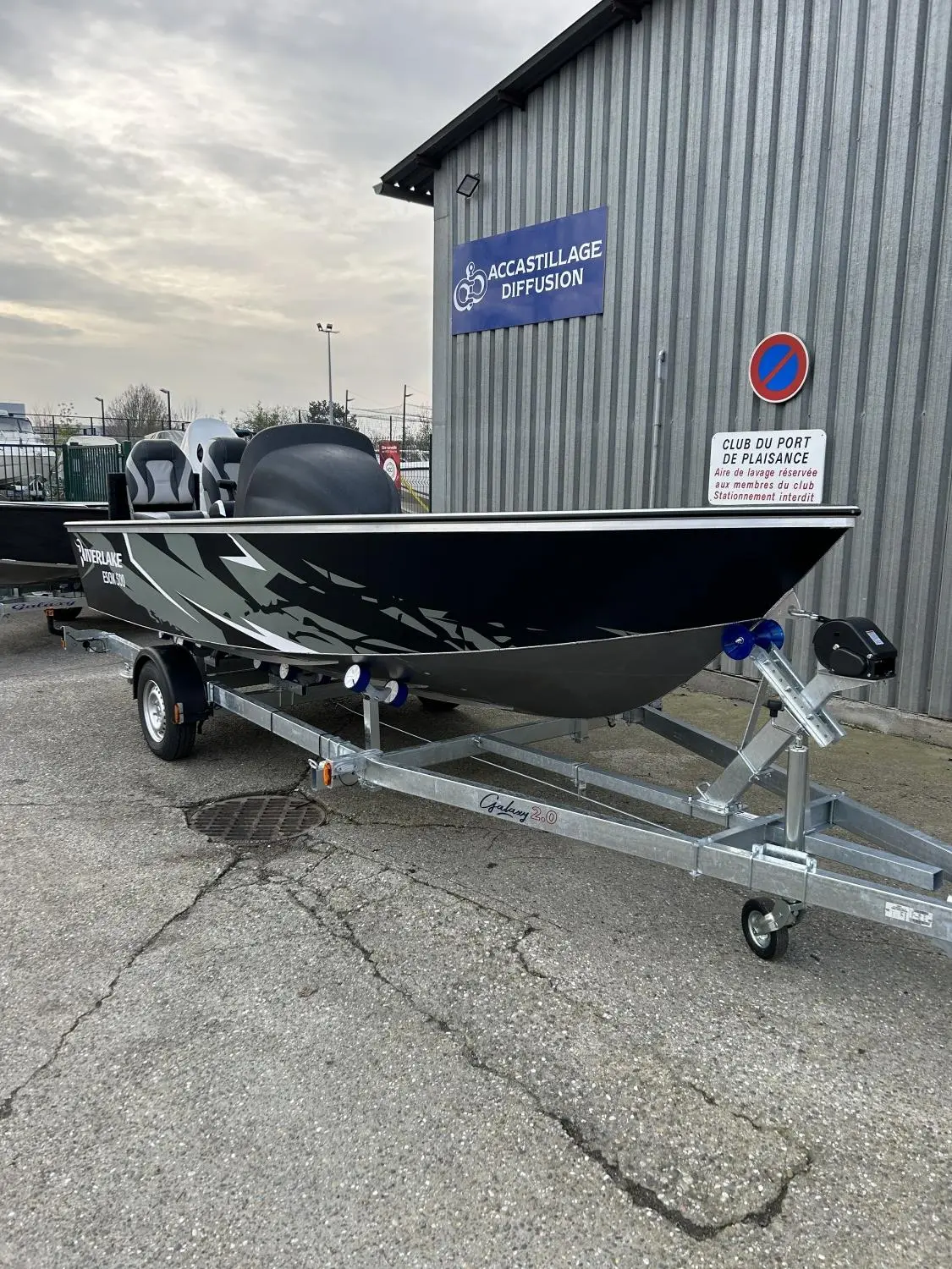 Riverlake 500 Esox Sc — Bateau à moteur noir et gris présenté sur sa remorque devant un bâtiment industriel.