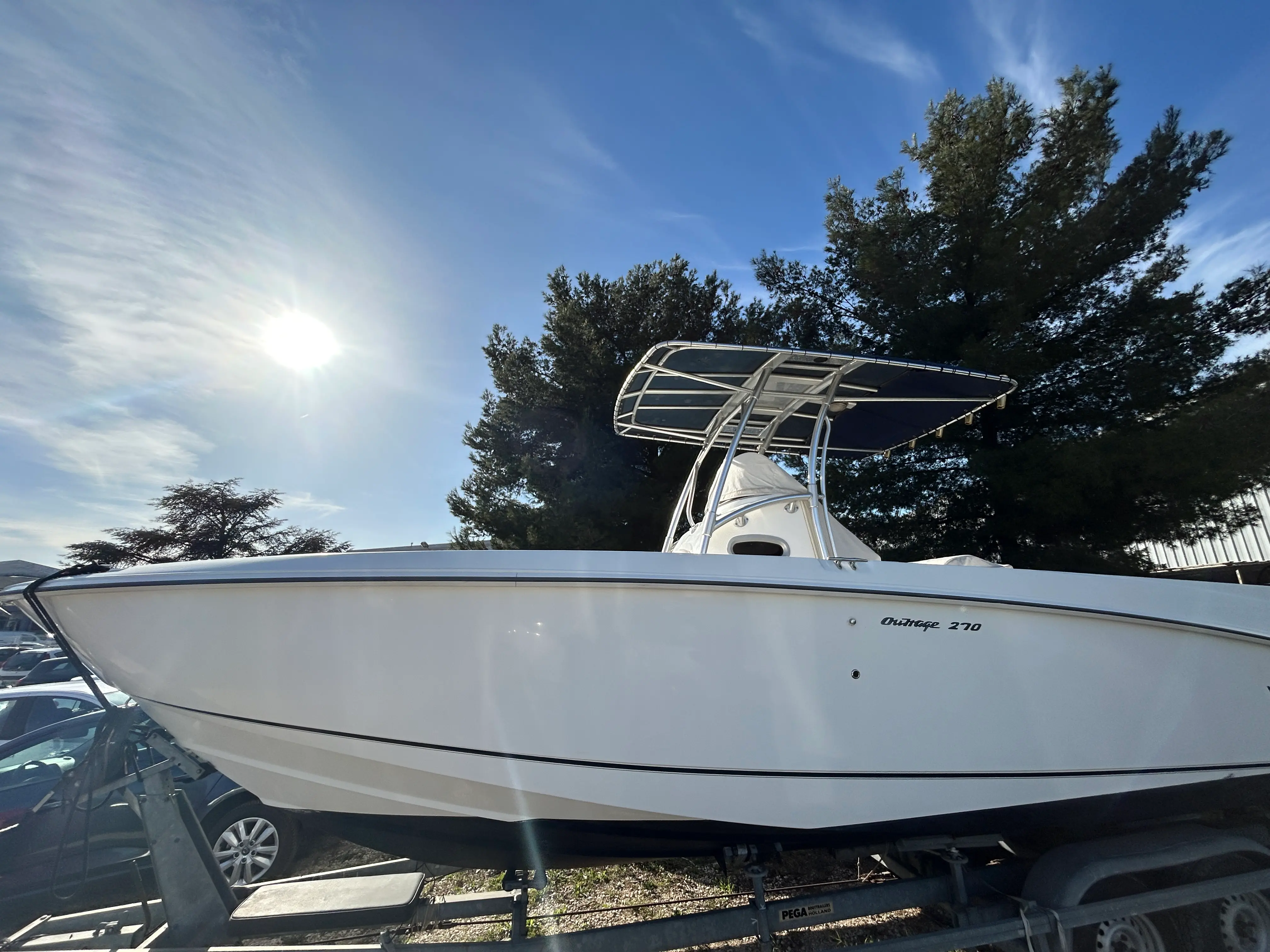 Boston Whaler 270 Outrage — Vue latérale d’un bateau blanc sur remorque, avec console centrale et T-top.