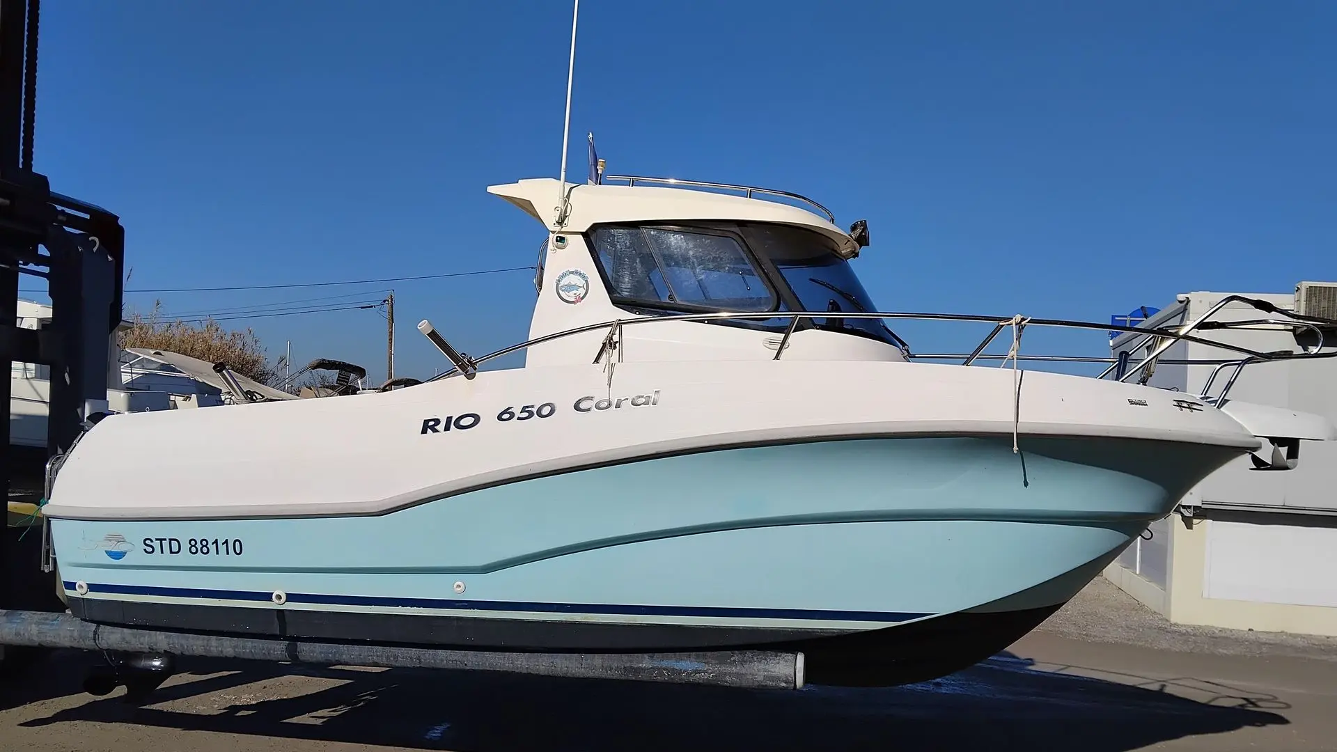 Rio 650 Coral — Bateau à moteur blanc et bleu présenté sur remorque, vu de profil par temps ensoleillé.