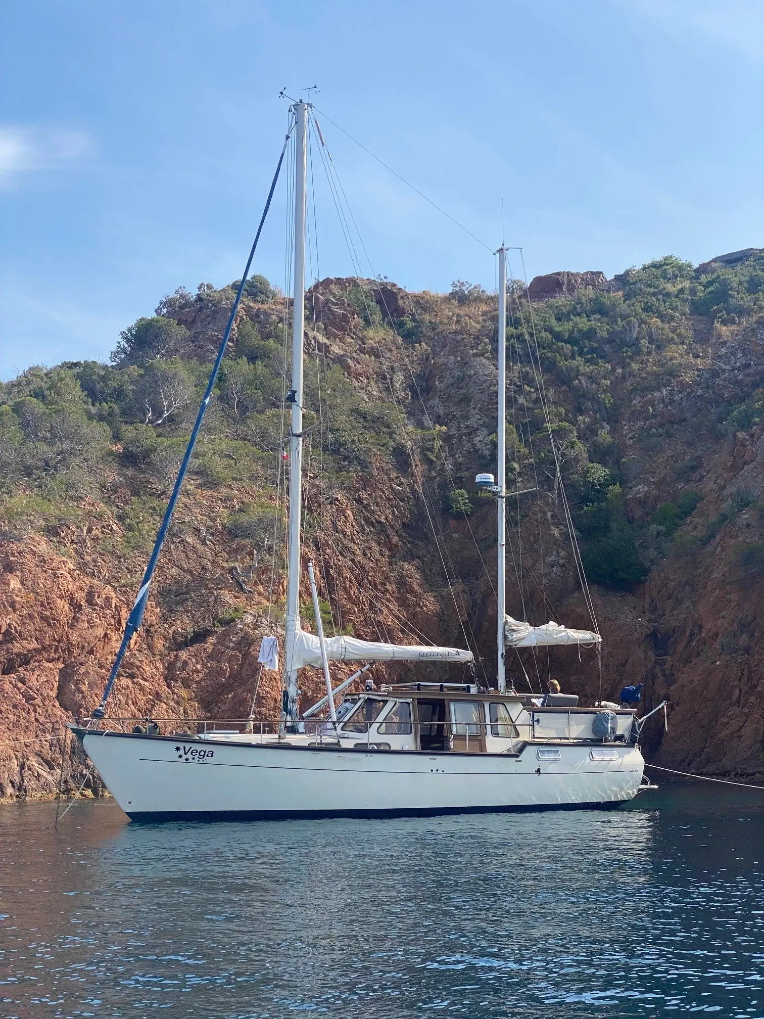 Siltala Yachts Nauticat 38 Ketch — Voilier blanc photographié au mouillage devant une côte rocheuse.