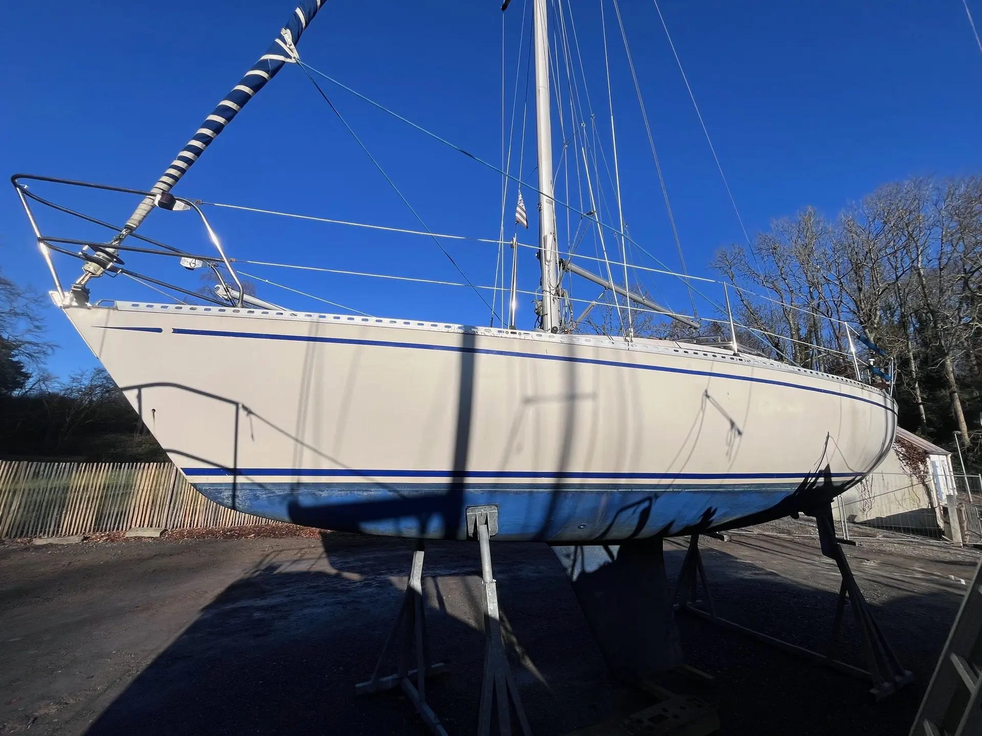 Beneteau First 28 — Voilier blanc à liserés bleus, posé sur berceau à terre par temps ensoleillé.