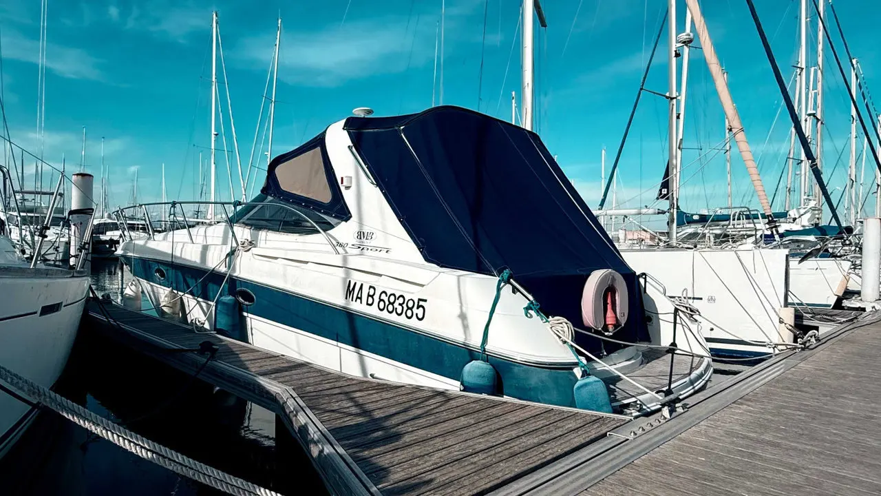 Bavaria 380 Sport Ht — Bateau à moteur blanc et bleu amarré dans un port, vu de trois quarts arrière.