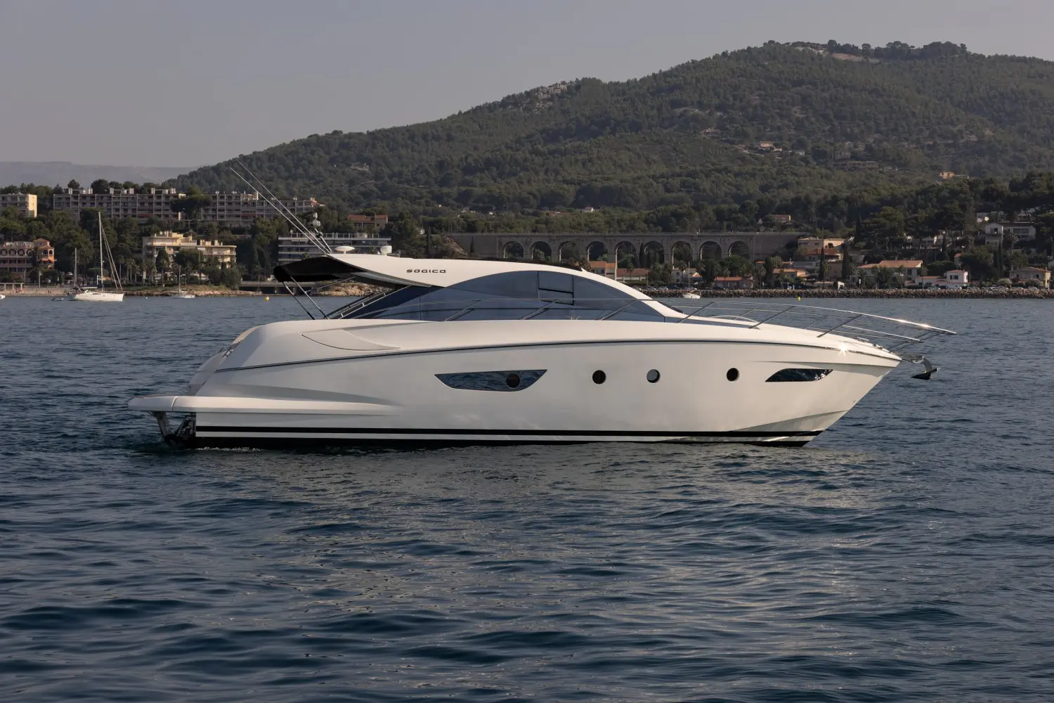 Sogica 47 Openbridge — Bateau à moteur blanc vu de profil sur l’eau, avec une colline en arrière-plan.