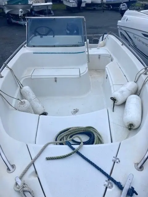 Jeanneau Cap Camarat 475 — Vue du cockpit ouvert d’un bateau blanc amarré, avec pare-brise, banquettes et cordages.