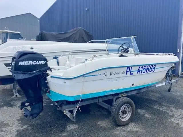Jeanneau Cap Camarat 475 — Bateau à moteur blanc et turquoise sur remorque, photographié devant un bâtiment industriel.