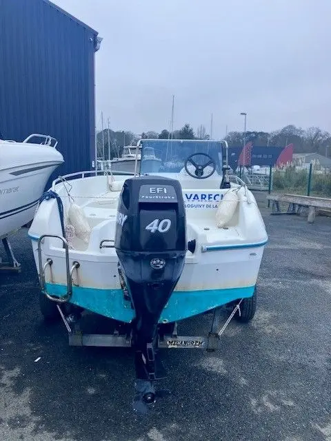 Jeanneau Cap Camarat 475 — Vue arrière d’un bateau à moteur blanc et turquoise, stationné sur sa remorque.