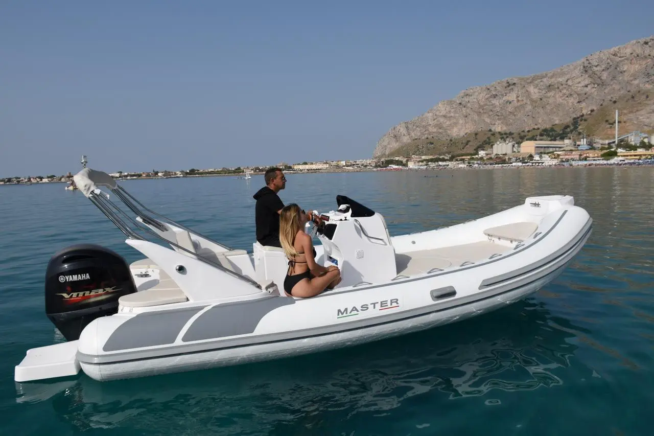 Master 630 Summer — Bateau semi-rigide blanc avec deux personnes à bord, au large d'une côte rocheuse.