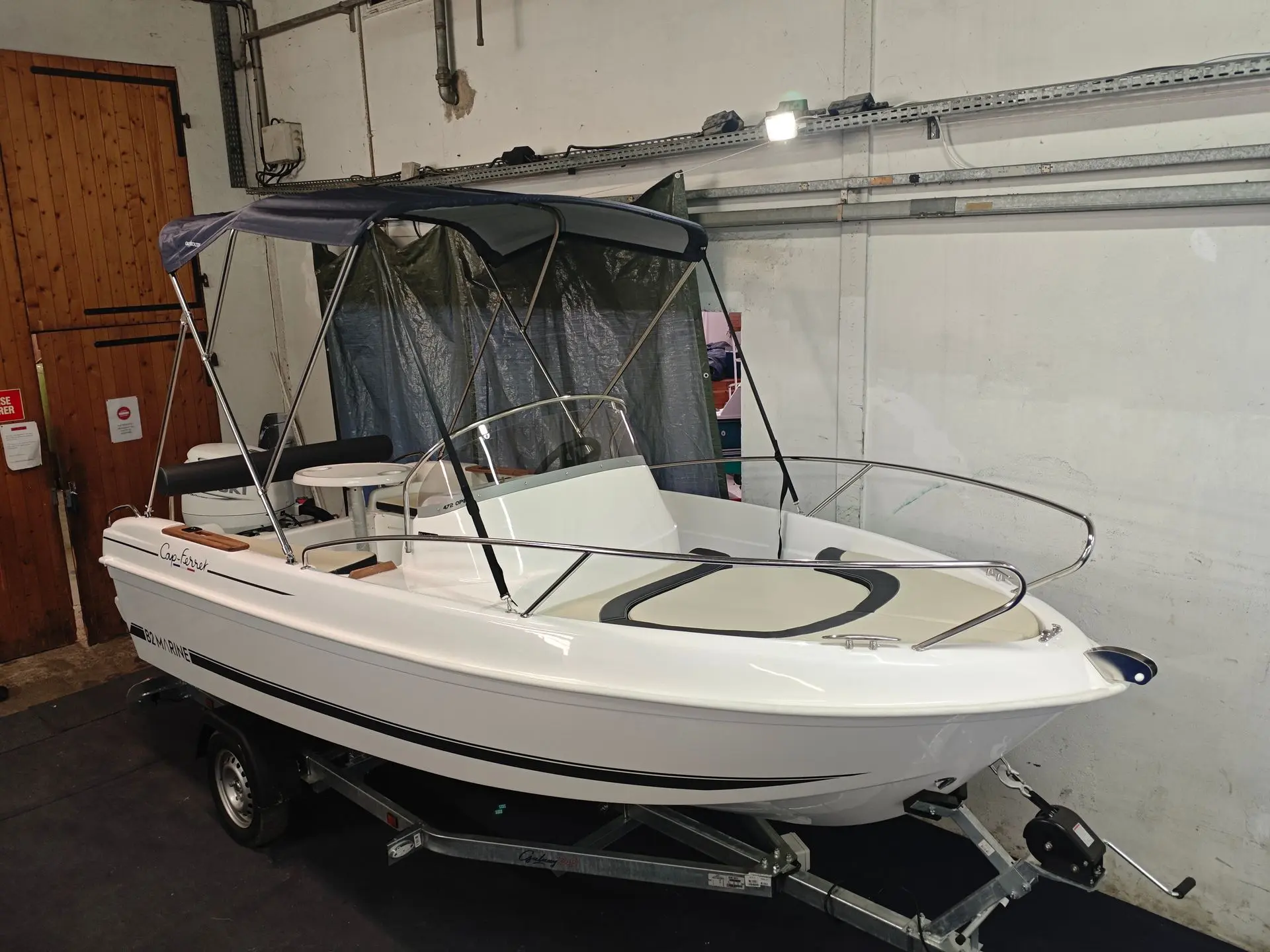 B2 Marine 472 — Bateau à moteur blanc avec taud de soleil, présenté sur remorque dans un garage.