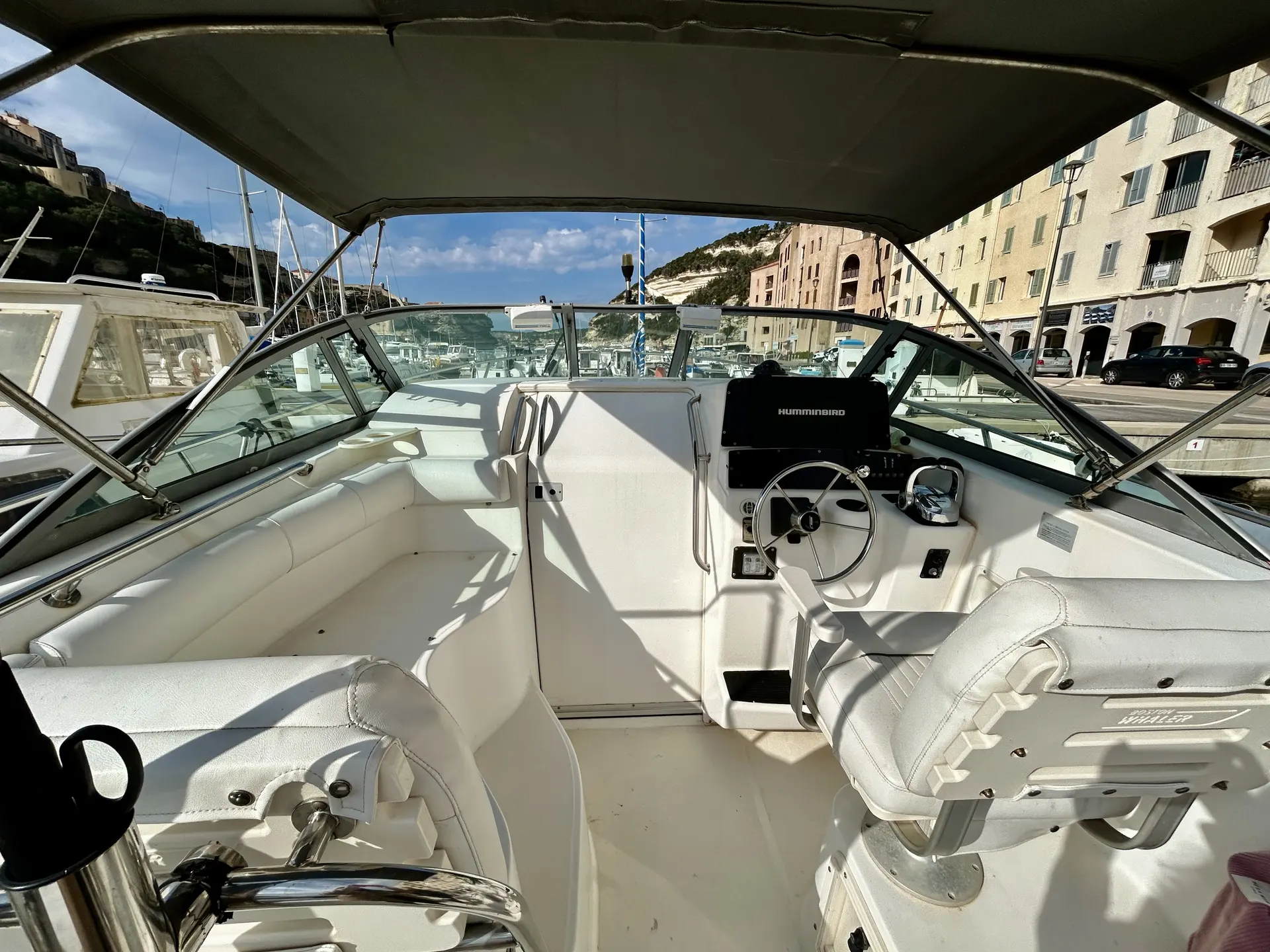 Boston Whaler 28 Conquest — Poste de pilotage et sièges du cockpit d’un bateau sous taud, dans un port.