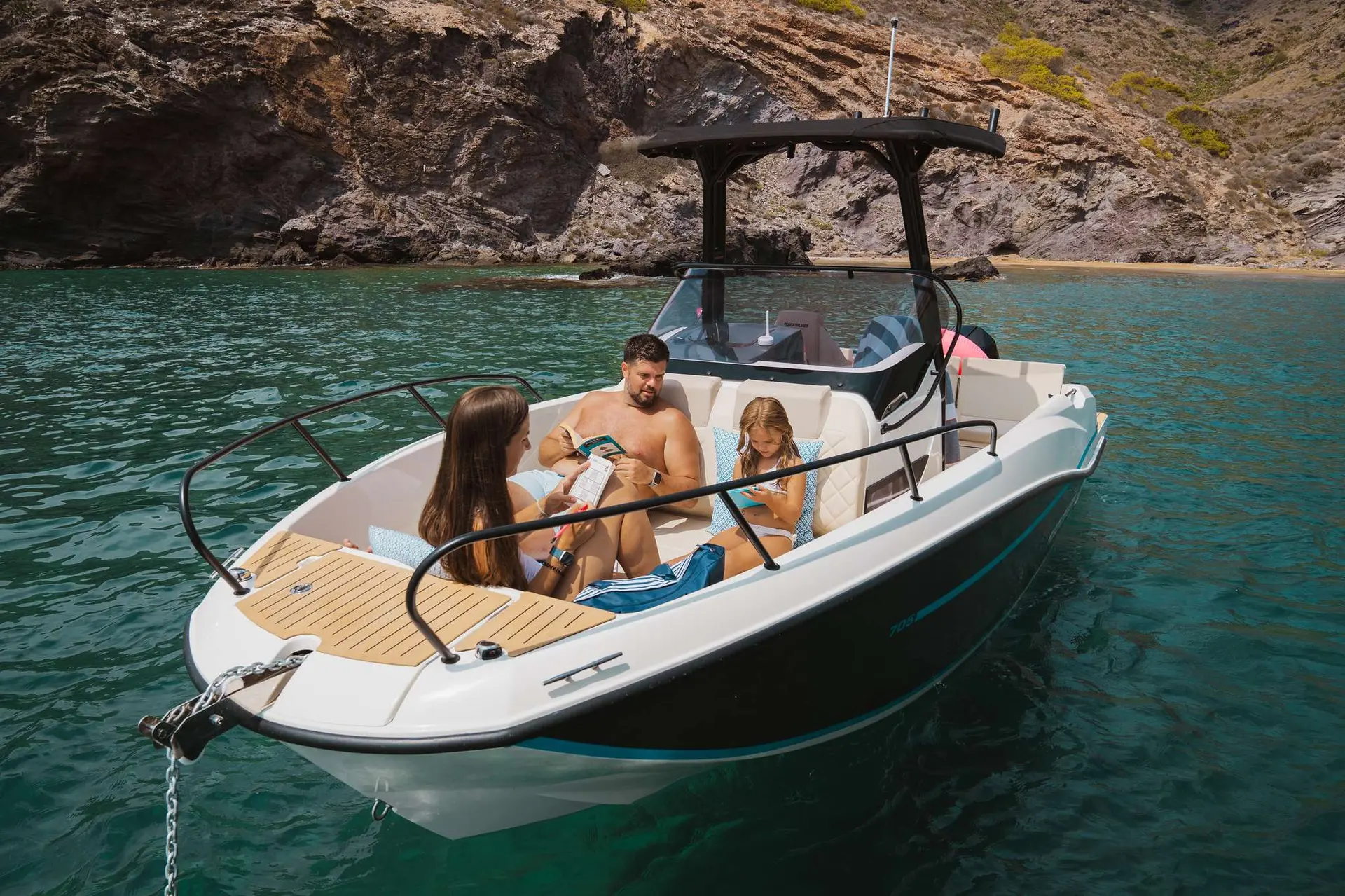 Quicksilver Activ 705 Cruiser — Bateau à moteur blanc et noir avec trois personnes, amarré dans une crique rocheuse.